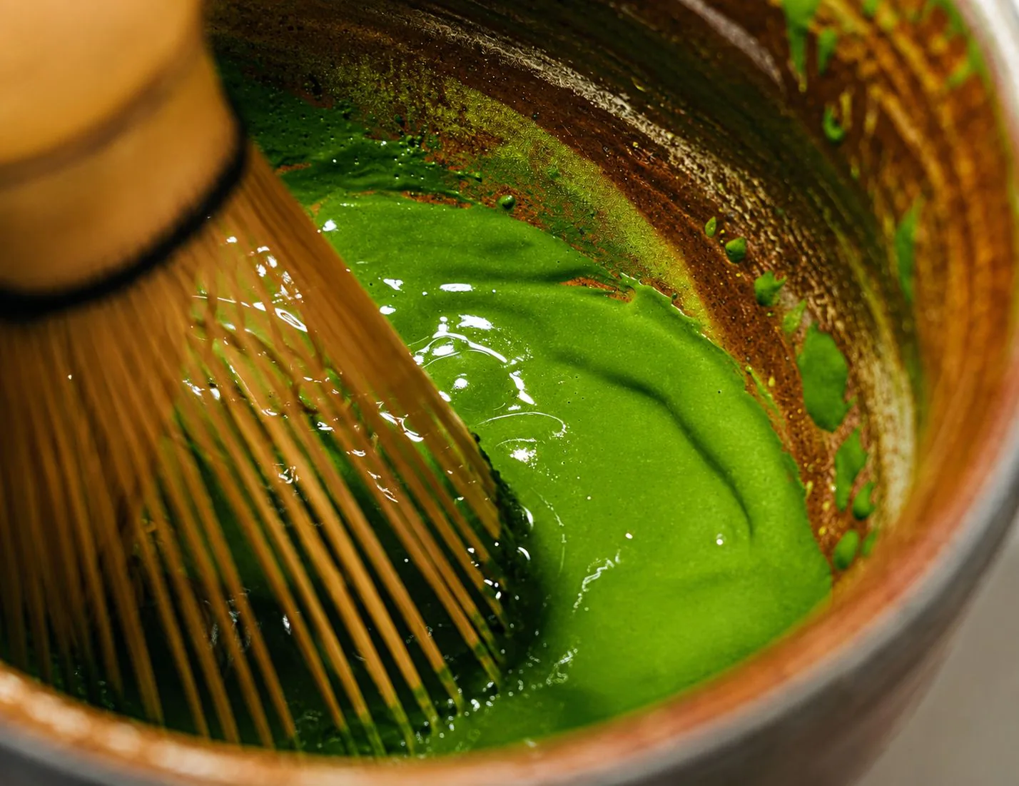 Un matcha fouetté dans un bol en céramique avec un chasen en bambou